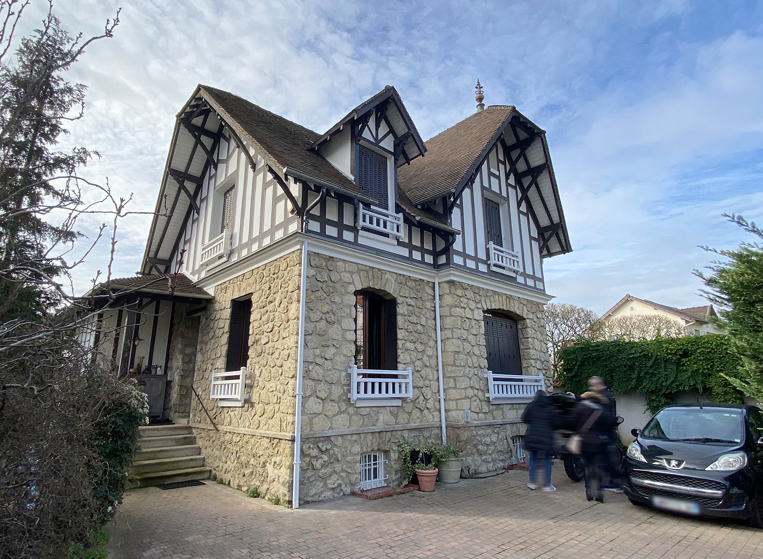La maison, pavillon meulière, volets noirs, balcons bois blanc, colombages, dallage pavés.